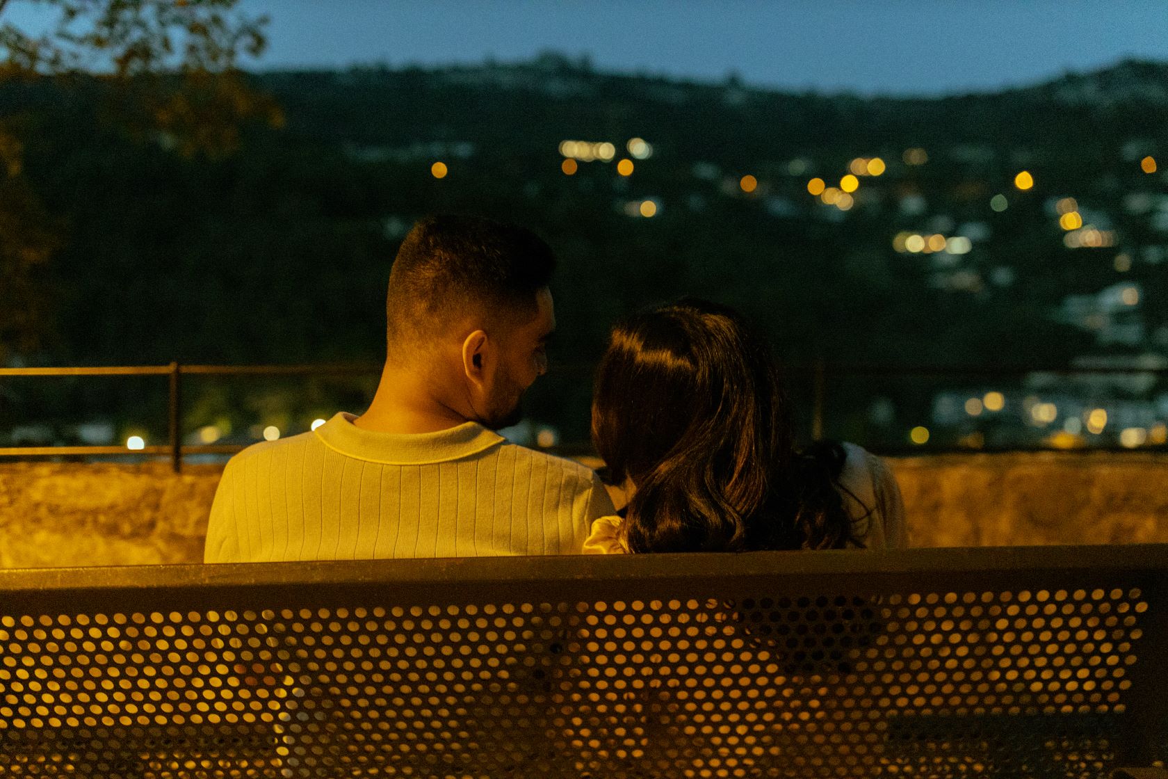 Couple de dos le soir, assis sur un banc et eclairé par une lumière orange